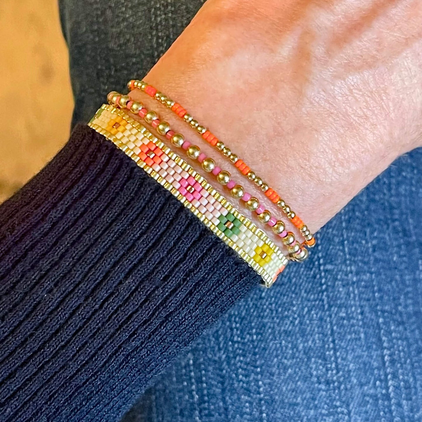 Seed bead flower bracelet set with pink, orange, green and yellow seed beads. Stacked with 2 gold ball stretch bracelets with small pink and orange seed beads.