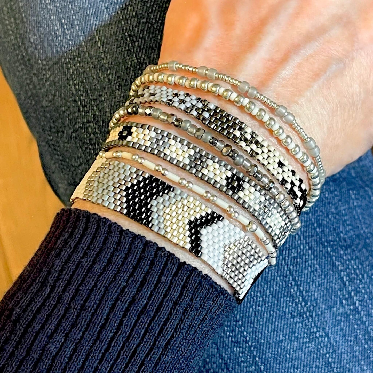 Sleek and modern black, white, and silver beaded boho bracelet stack of 7. With woven seed bead peyote bracelets and stretch bracelets.