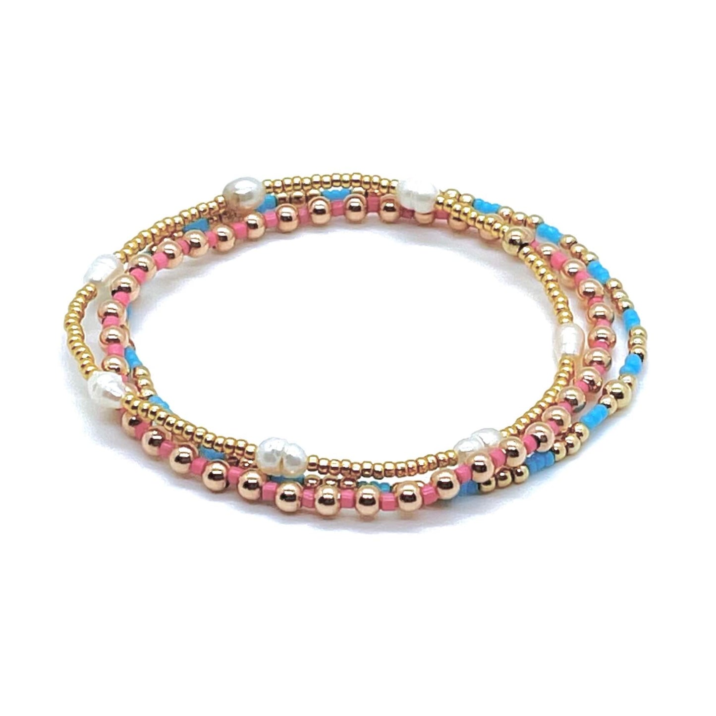 Stack of 3 dainty gold ball, freshwater pearl, and pink and light blue seed bead stretch bracelets for women.