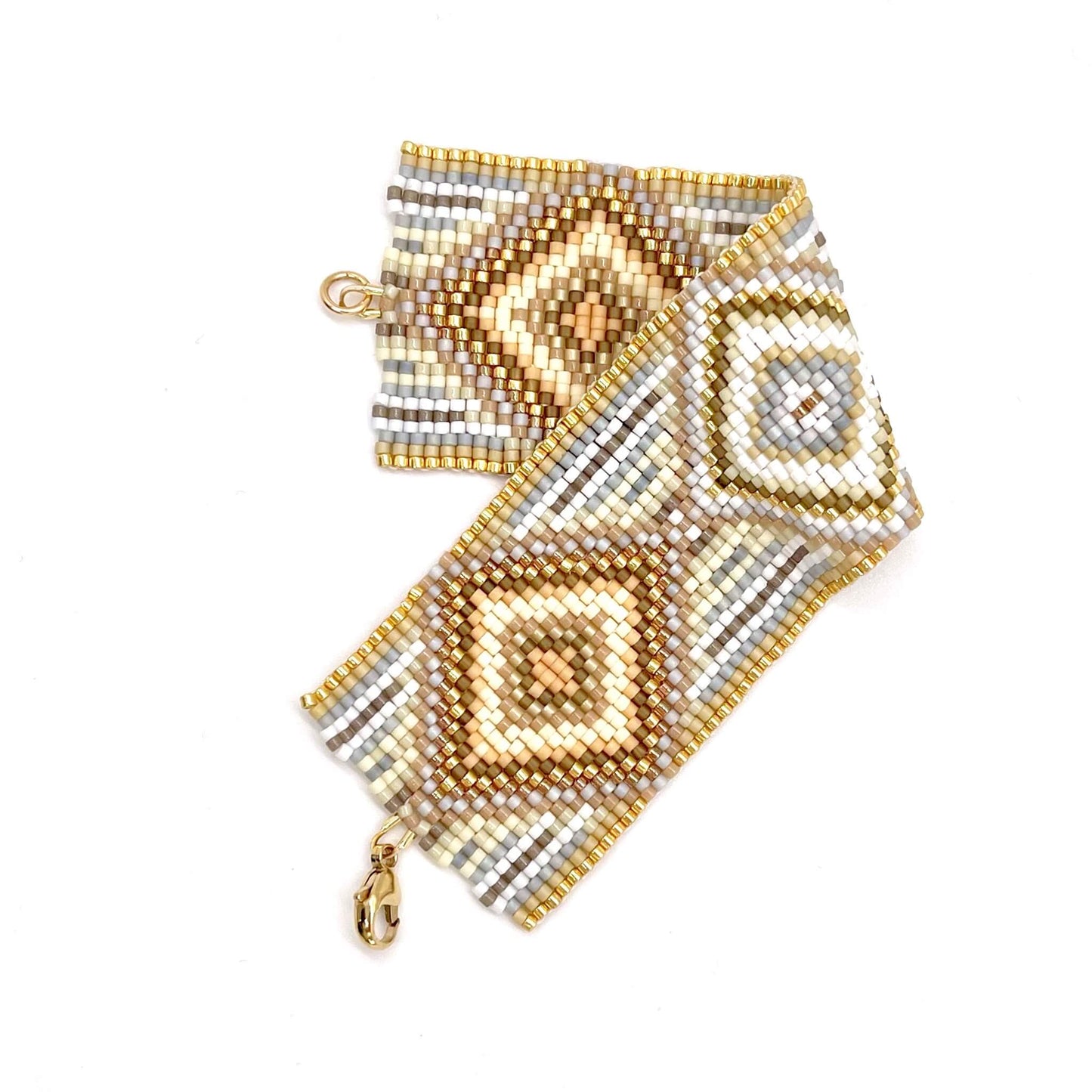 Wide hand woven peyote beaded bracelet with clasp in an intricate diamond and stripes pattern of white, tan, and gold beads.