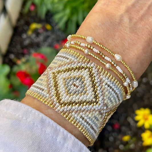 Beaded bracelet set with wide seed bead bracelet cuff in white, gold, and tan diamonds, stacked with 3 gold, pearl and seed bead stretch bracelets.