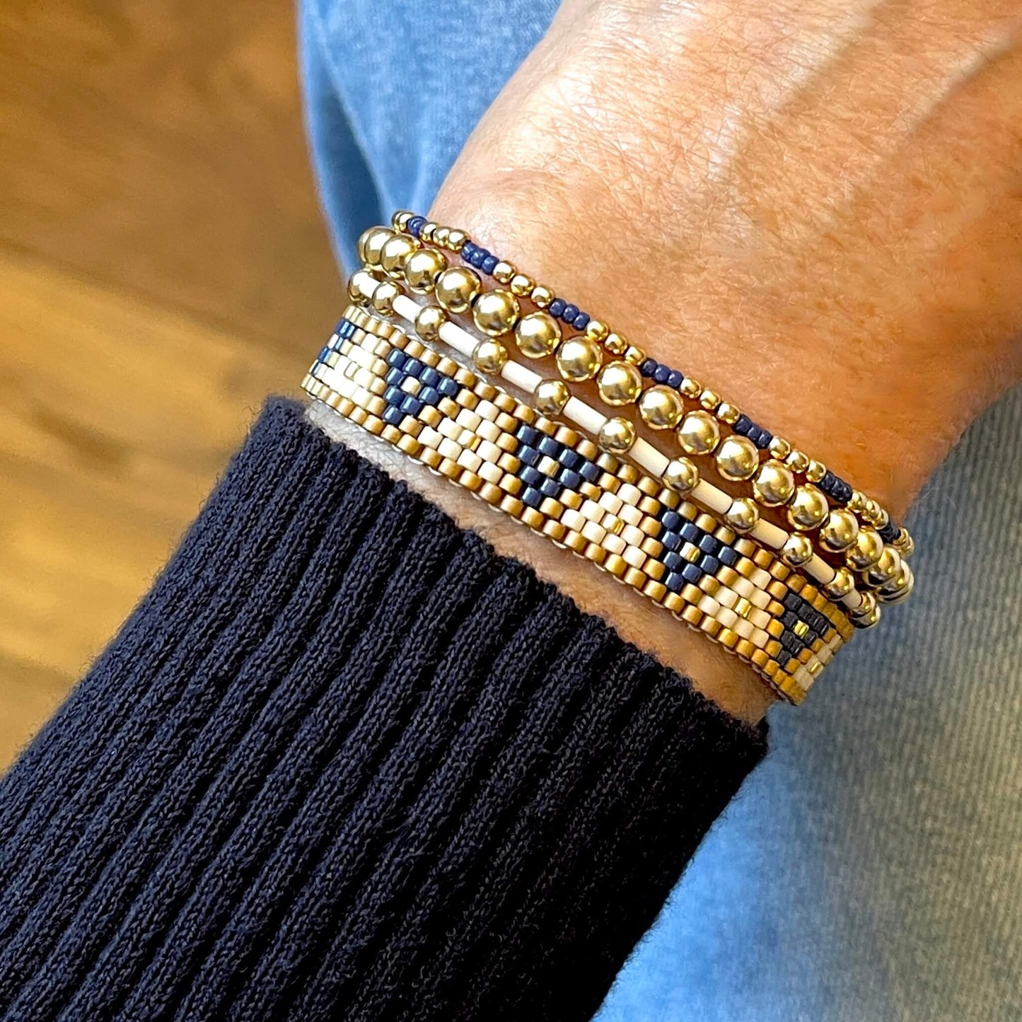 Women's blue, white, and gold beaded bracelet stack with woven triangle band and 3 gold ball stretch bracelets.