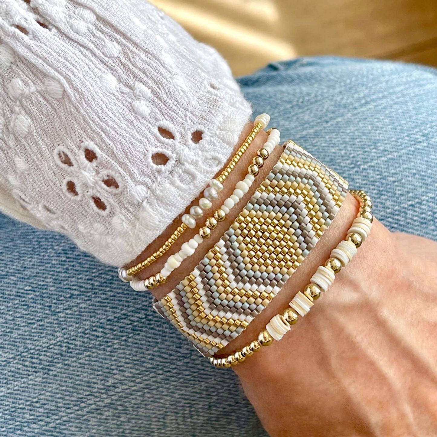 Beaded bracelet white and gold wristband stack with woven and stretch bracelets made from seed beads, freshwater pearls, heishi beads, and gold balls.