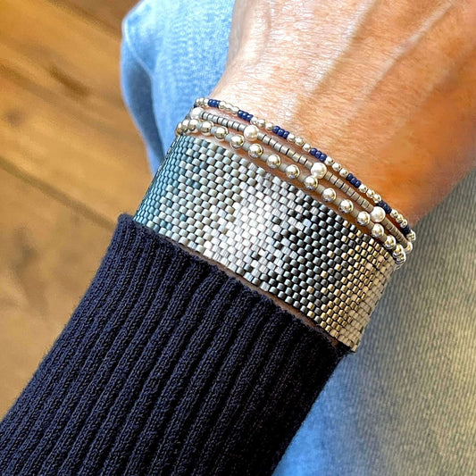 Blue and grey beaded bracelet stack with a peyote stitch ombre cuff bracelet and 3 silver and pearl ball stretch bracelets.