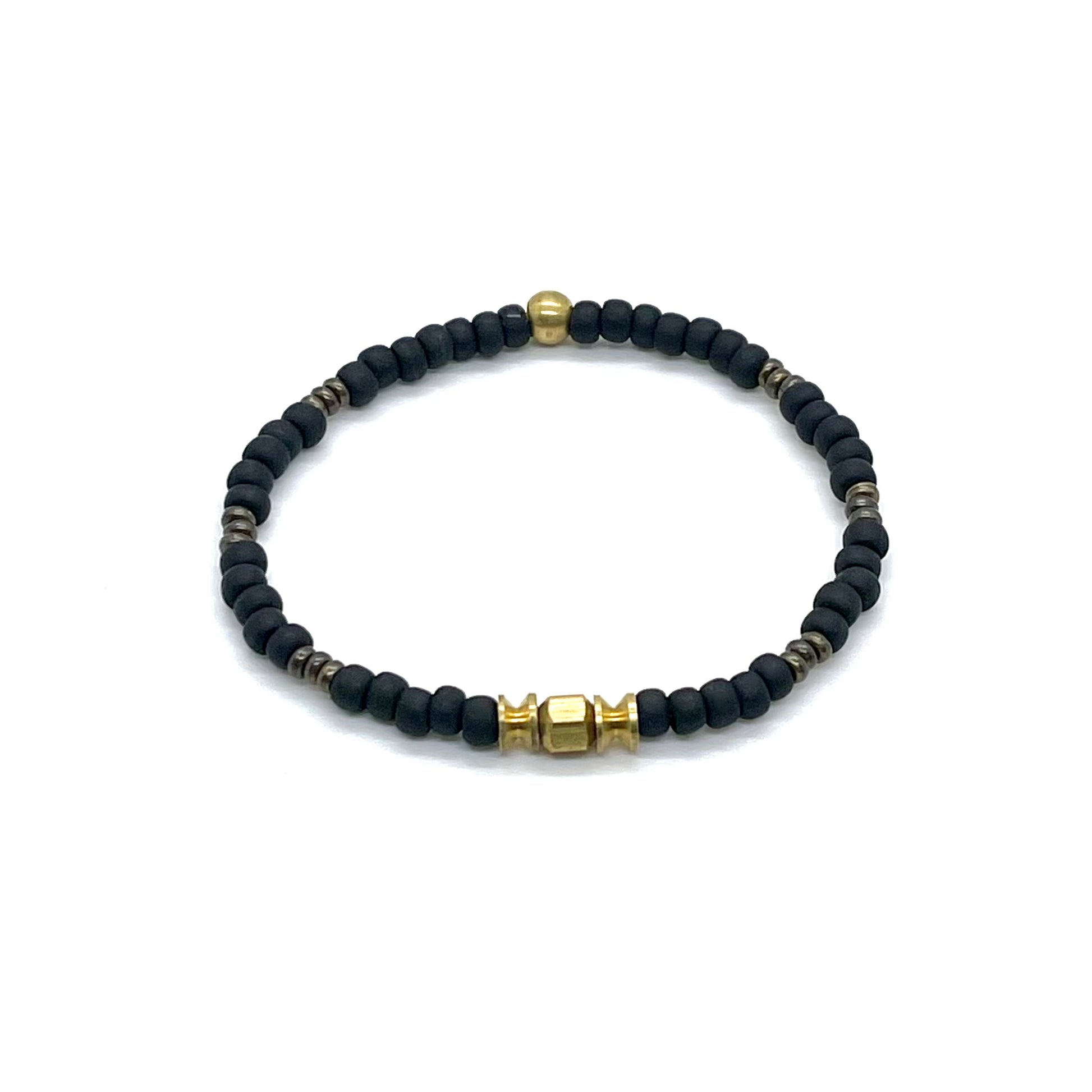 Brass bracelet with matte black seed beads, raw brass cylinders, and brass-plated disk beads on elastic stretch cord.