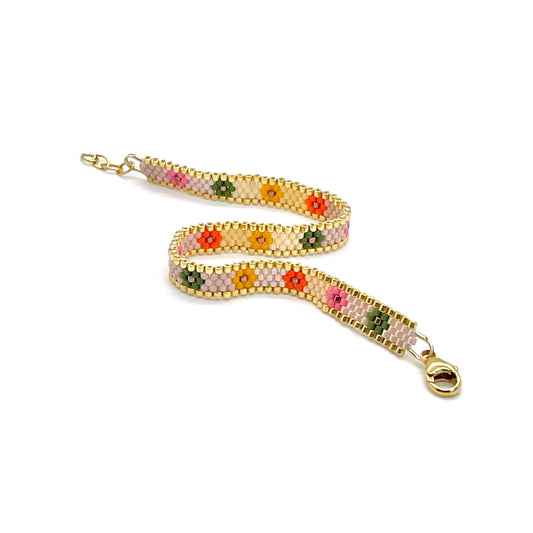 Brightly colored thin beaded bracelet cuff with flowers in green, pink, orange, and yellow on a light cream background with a gold trim.