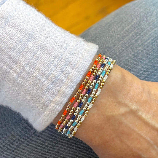 Colorful, dainty round seed bead gold and silver stretch bracelets in orange, pink, blue, or white.