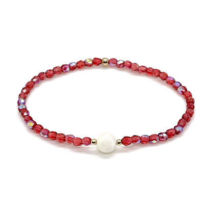 Coral-red crystal bracelet with a mother-of-pearl center bead and small gold accent beads.