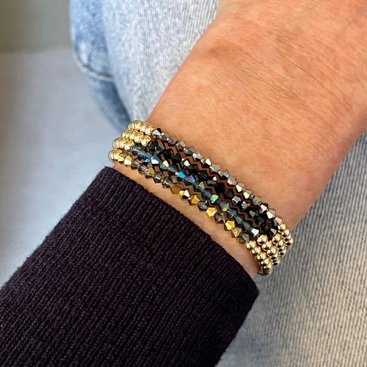 Dainty gold stretch bracelets with a center bar of mini crystal beads in four sparkly colors: gold, blue, black, and hematite.