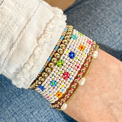 White woven and gold stretch beaded bracelet stack with brightly colored seed bead flowers and pearl, and gold filled beads.