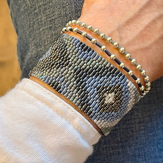 Wide hand woven bracelet with blue & silver seed beads, layered with 2 sterling silver ball beaded stretch bracelets.