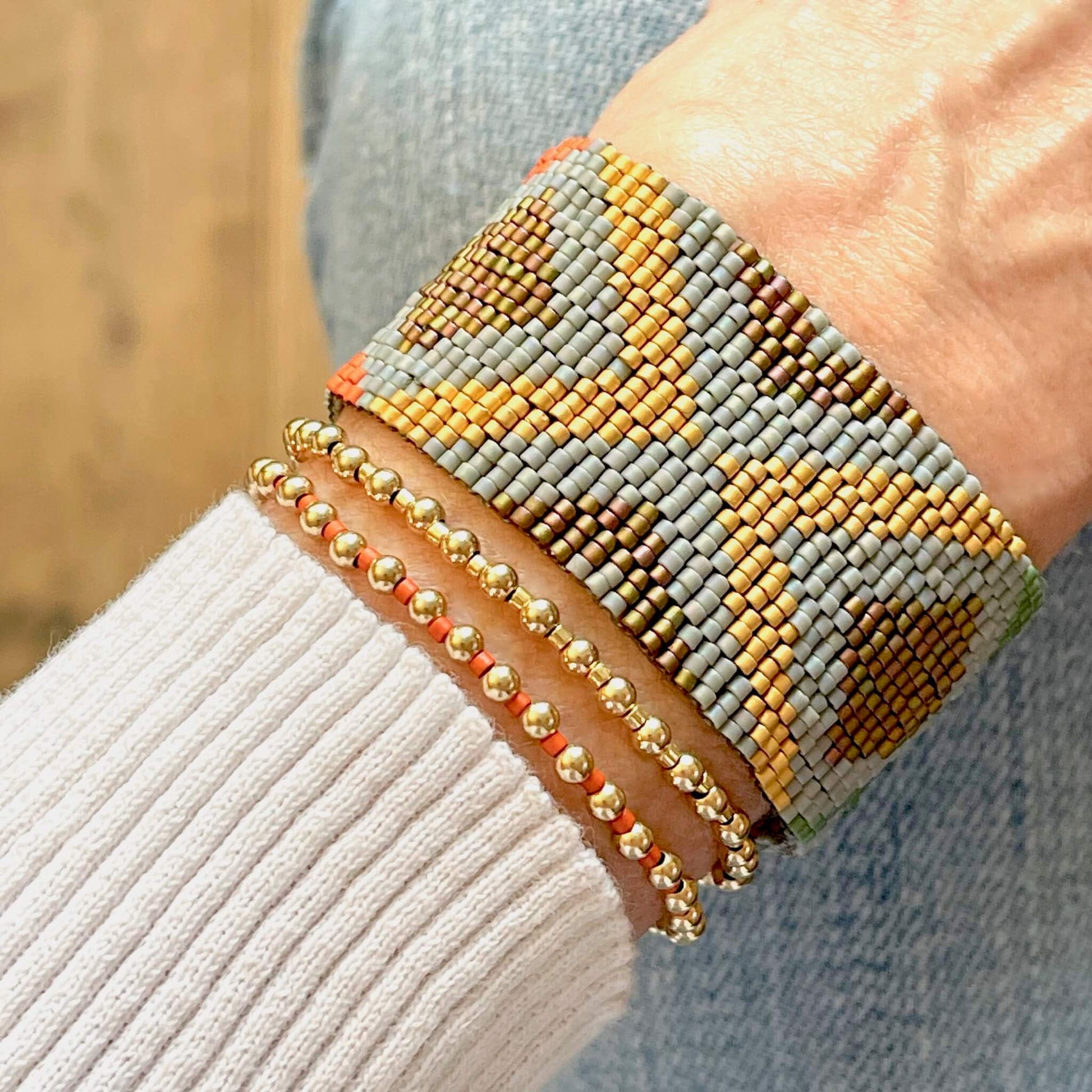 Wide hand woven bracelet with gray, gold, orange, & green miyuki beads, layered with 2 gold fill ball beaded stretch bracelets.