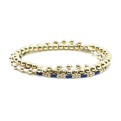 Gold ball bracelet stack with blue and white alternating seed beads on elastic stretch cord.