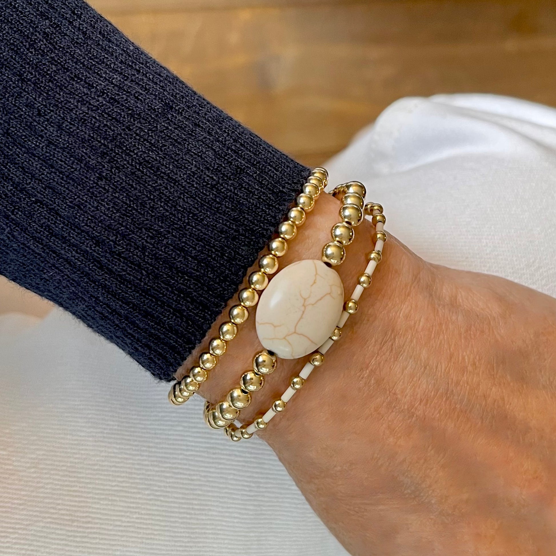 Gold ball bracelet stack of 3 with puff oval magnesite stone and white bugle beads on elastic stretch cord.