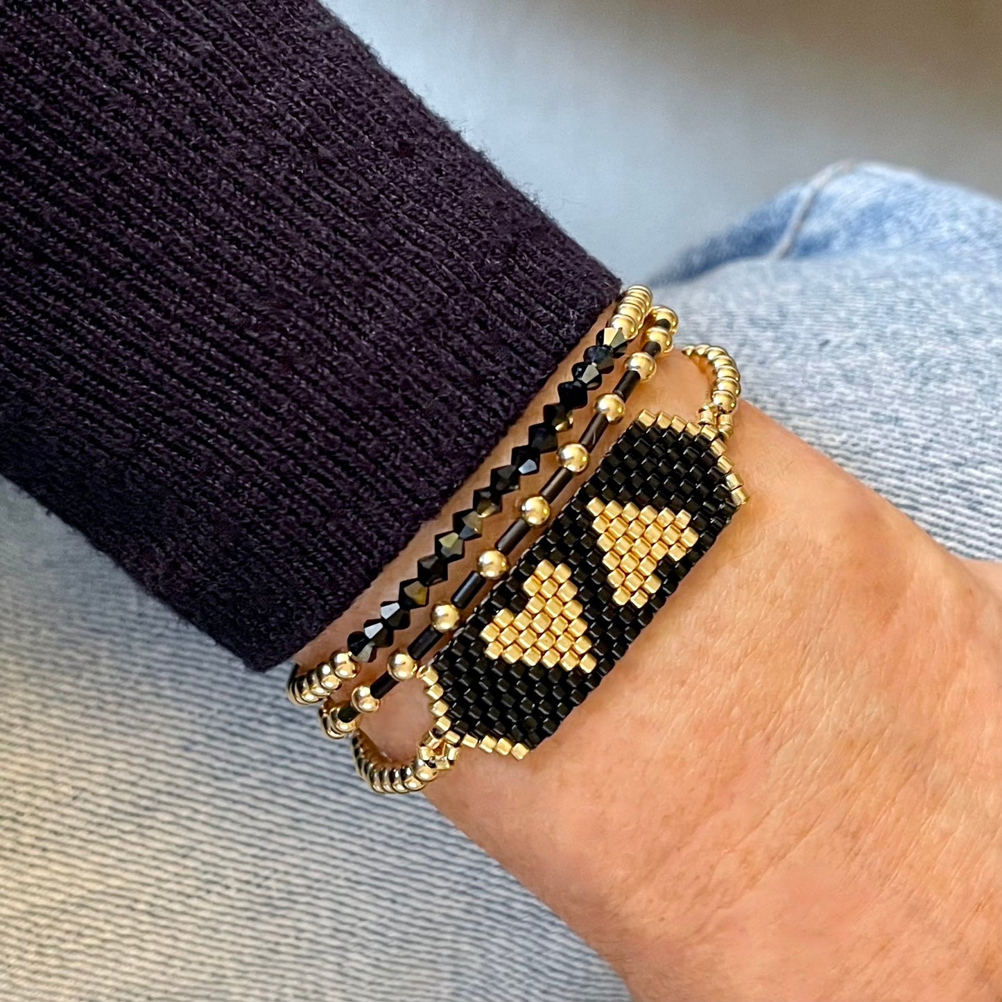 Gold and black crystal and seed bead bracelet stack with skinny stretch bracelets and heart band.