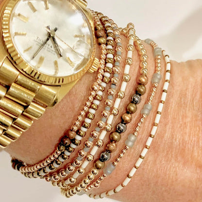 Gold and neutral tones beaded stretch bracelet stack of 7. With 14K rose and yellow gold fill beads, gray and white seed beads, and metallic beads.