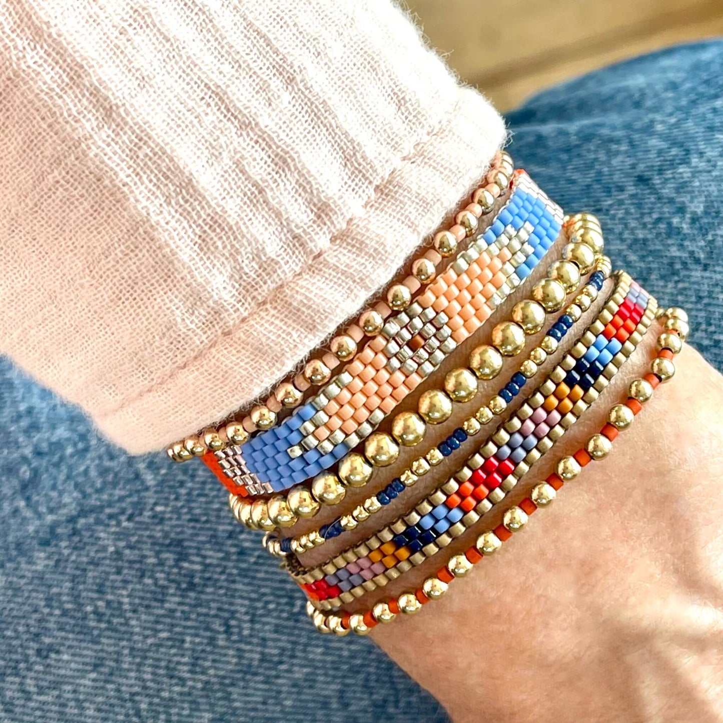 Gold southwest mix bracelet stack with 2 woven brands and 4 gold ball stretch bracelets. Handmade using orange, blue, red, and peach seed beads.