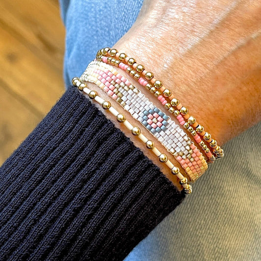 Handmade beaded bracelets with a pastel woven band and 3 gold ball stretch bracelets with ivory, pink, and peach seed beads.