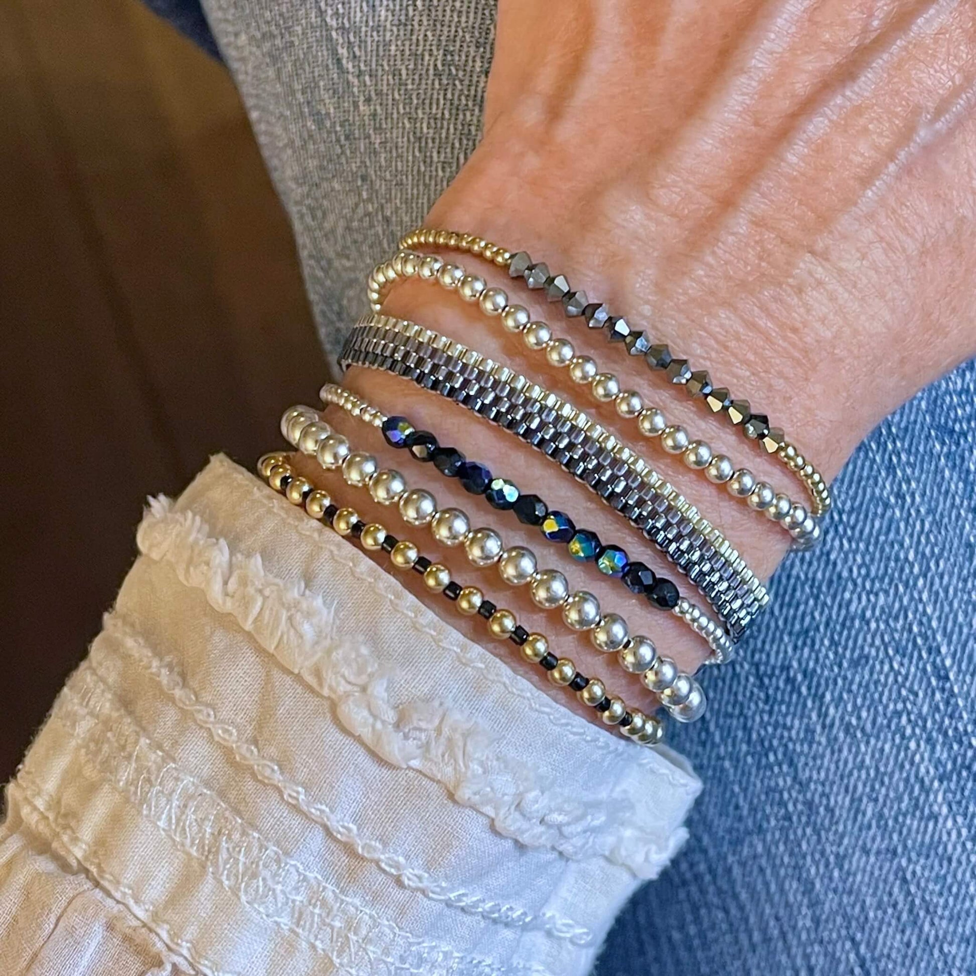 Handmade bracelets beaded with small metallic seed beads in a thin woven band, and silver, gold, and crystal stretch bracelets.
