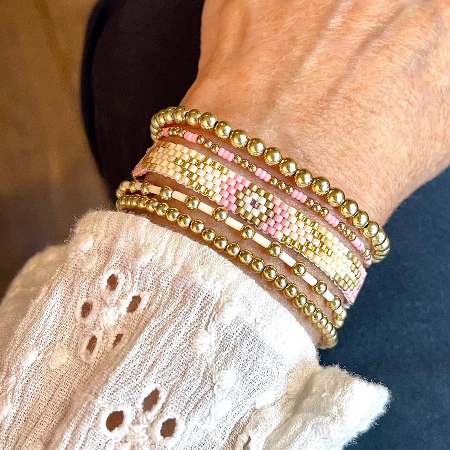 Handmade bracelets stack with a pink and ivory seed bead band and 4 gold ball stretch bracelets.