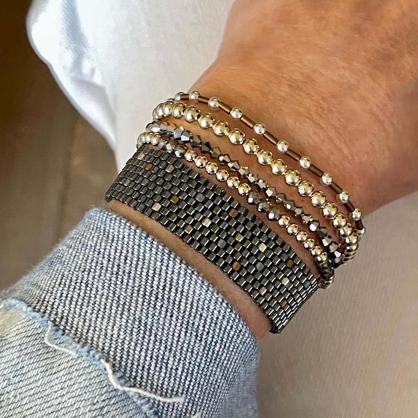 Bracelet stack with a gunmetal seed bead handwoven cuff and 4 mixed metal and crystal stretch bracelets.