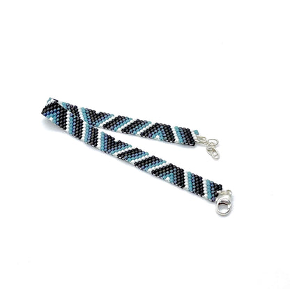 Hand woven men’s peyote beaded bracelet with clasp and blue, black, brown, & white seed beads in a stripes & triangles style.