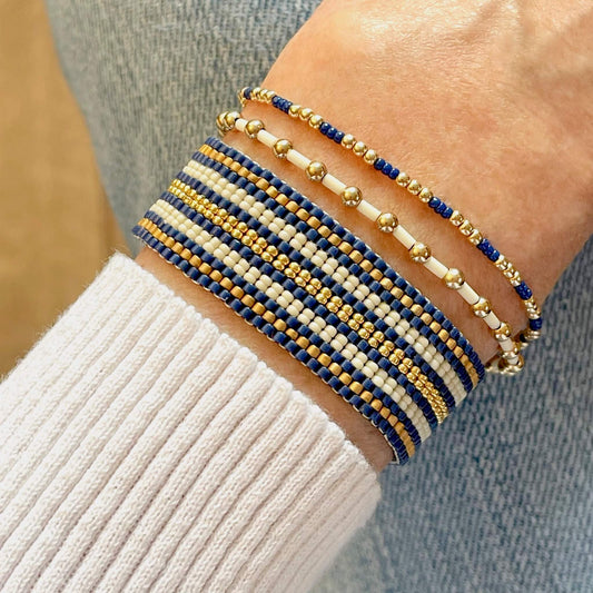 Crisp and classic nautical navy, ivory, and gold beaded bracelet stack of 3 with striped woven cuff and 2 gold ball stretch bracelets.