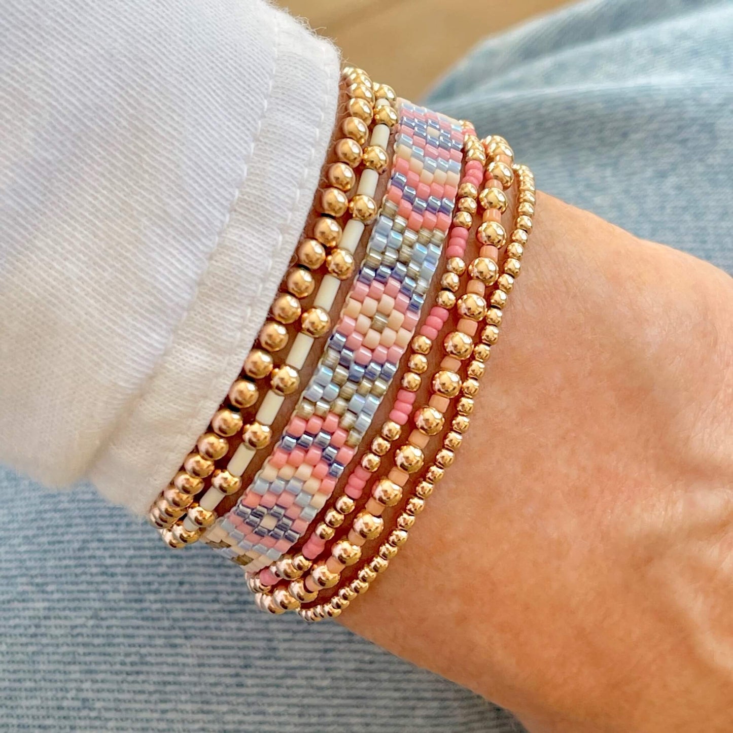Pink, peach, blue, and ivory beaded bracelet stack with 5 gold filled stretch bracelets and a thin woven arrow cuff band.