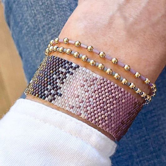 Purple, pink, and grey beaded bracelets with a peyote stitch ombre cuff and gold ball stretch bracelets. Handmade women's beaded bracelets.