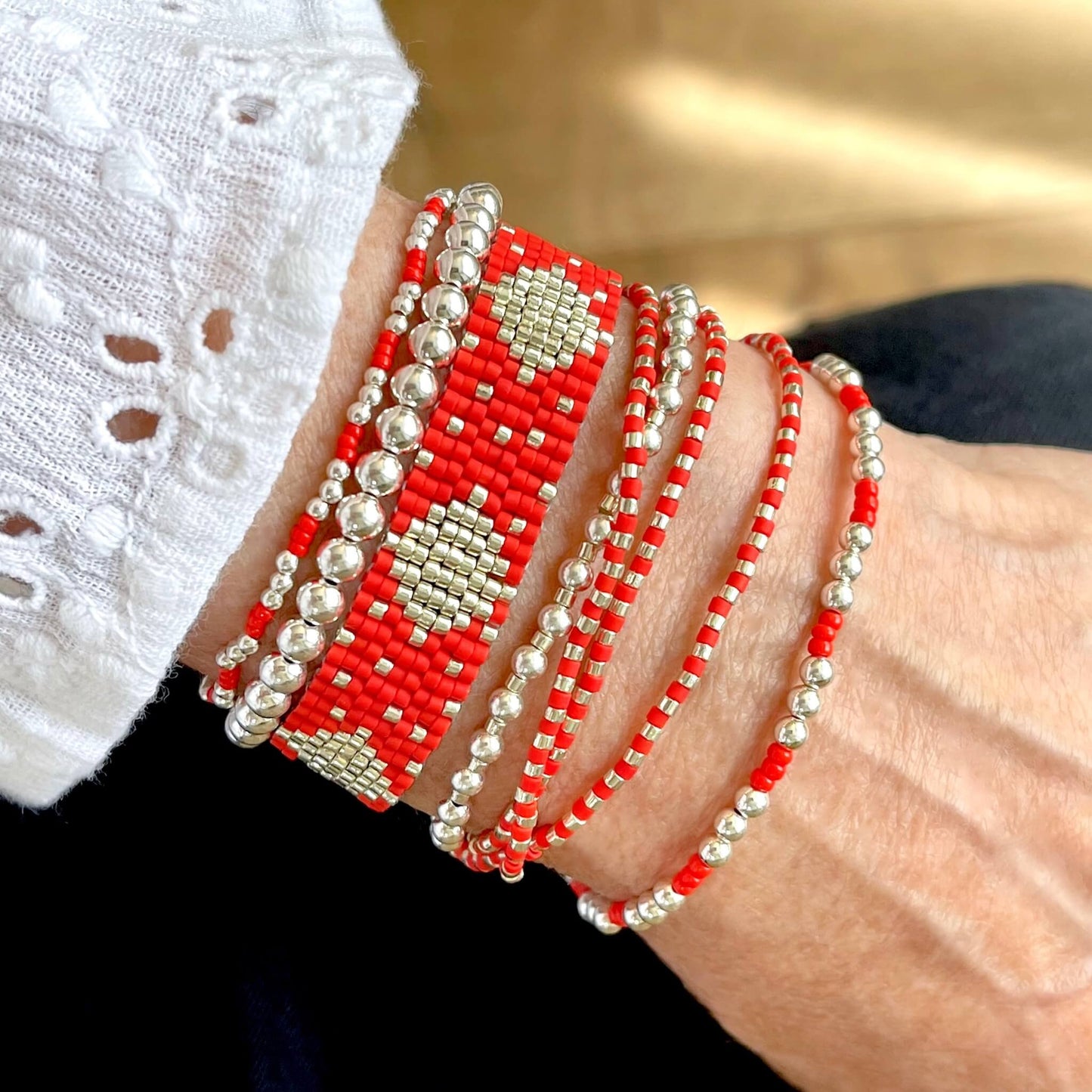 Red bracelets in a stack with a seed bead handwoven cuff and wrap, and sterling silver stretch bracelets.