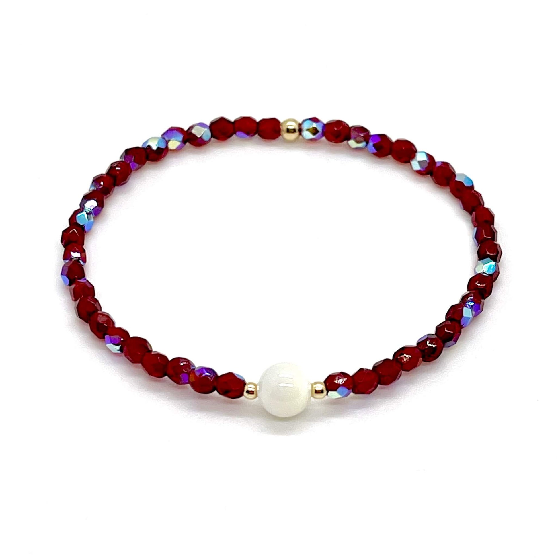 Red crystal bracelet with a mother-of-pearl center bead and small gold accent beads.