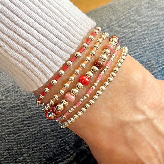 Silver stretch bracelet stack with red beads, pink beads, and seed beads.