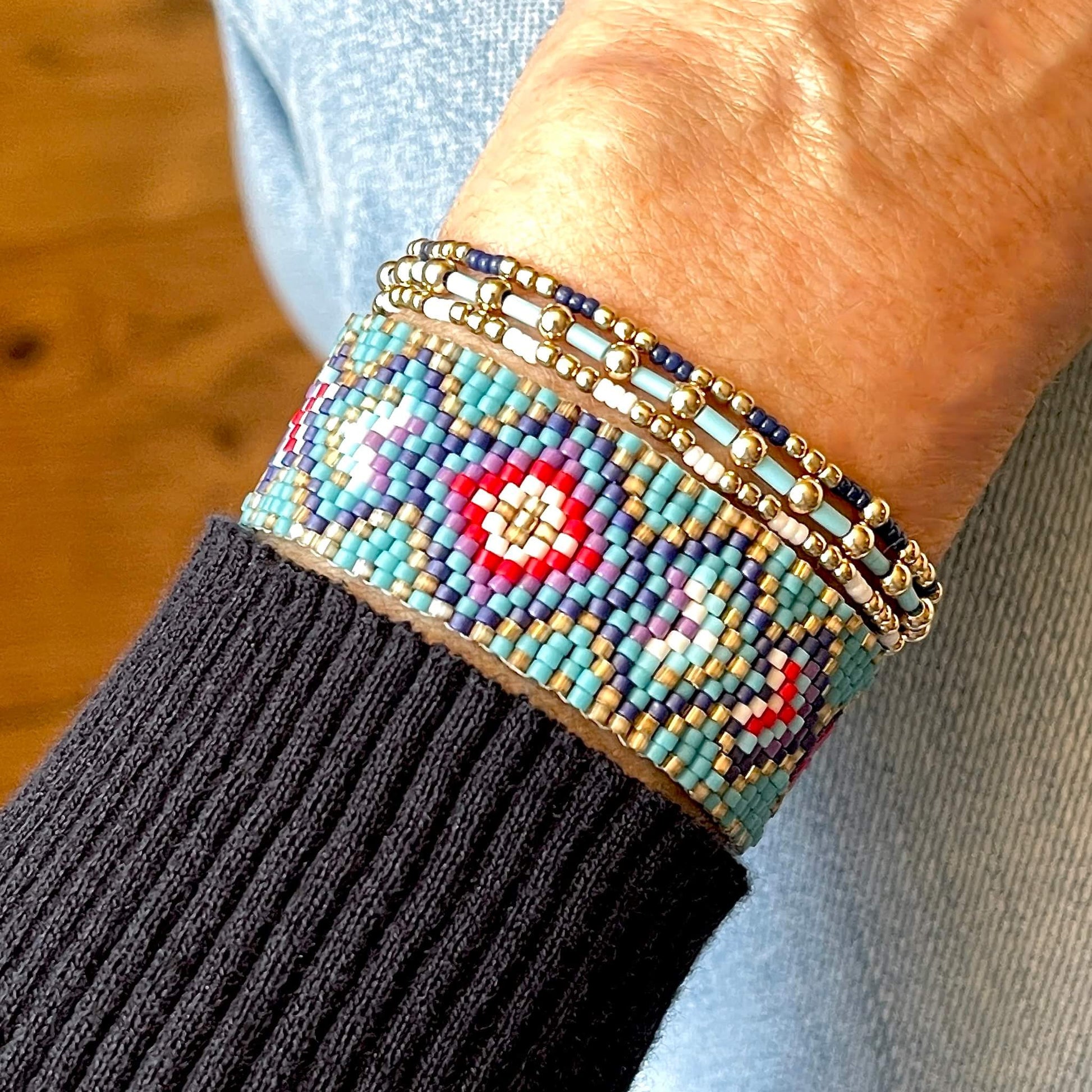 Seed bead cuff and stretch bracelet stack. A peyote band with turquoise, blue, and red diamonds, and 3 gold stretch bracelets with white, turquoise and navy beads.