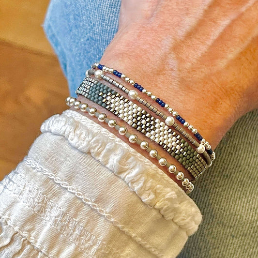 Silver and blue beaded bracelet stack with a thin woven band and 3 stretch bracelets. Sterling silver and pearl beads with glass seed beads.