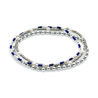 Silver bracelet stack with pearls, grey and blue seed beads, and silver ball beads on stretch cord.