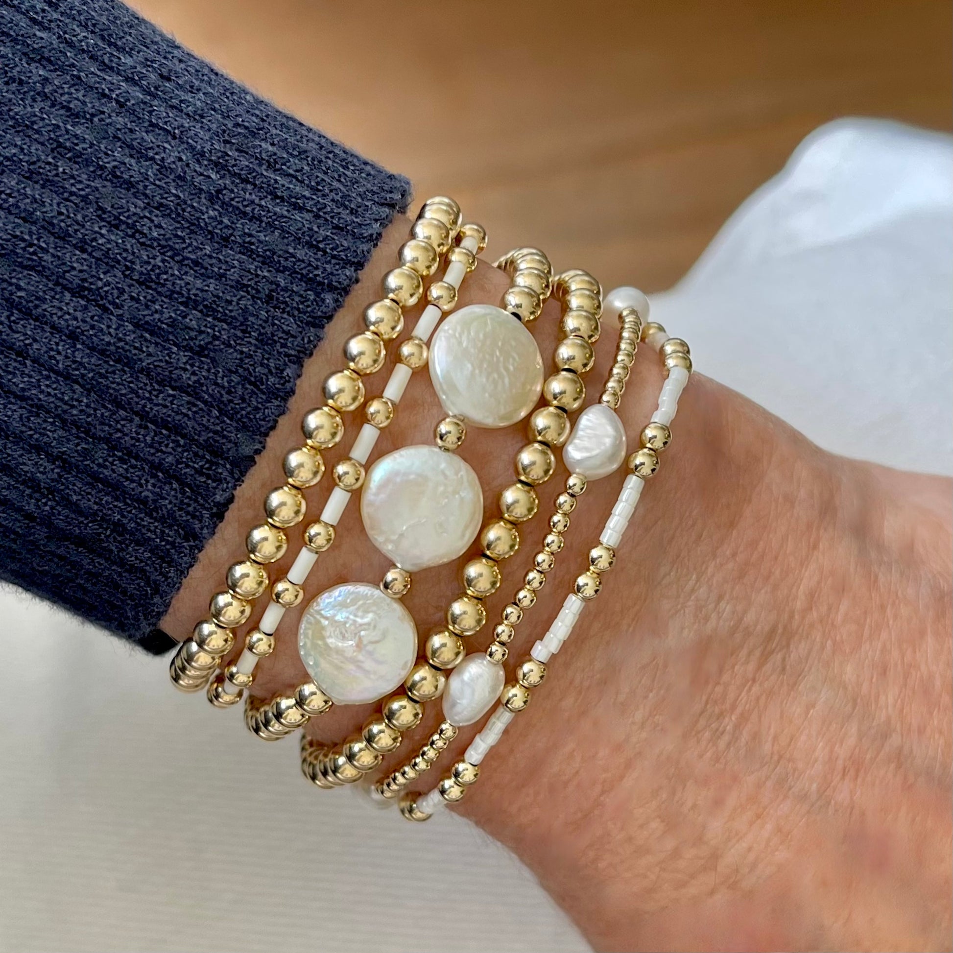 Stacked pearl bracelets with gold beads, freshwater rice and coin pearls, and white seed beads on stretch cord.