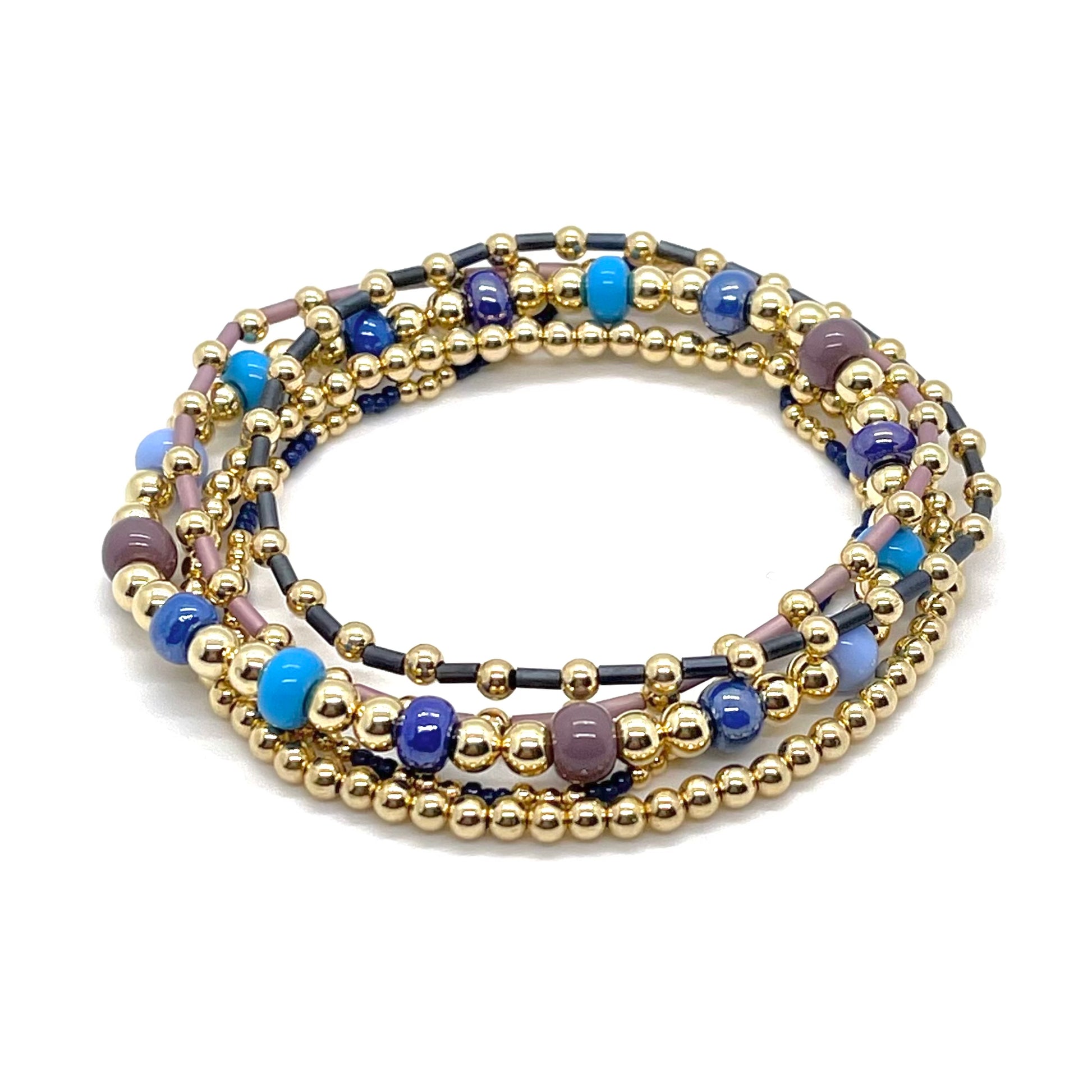 Summer gold bead bracelet stack with blue and mauve glass seed beads on stretch cord.