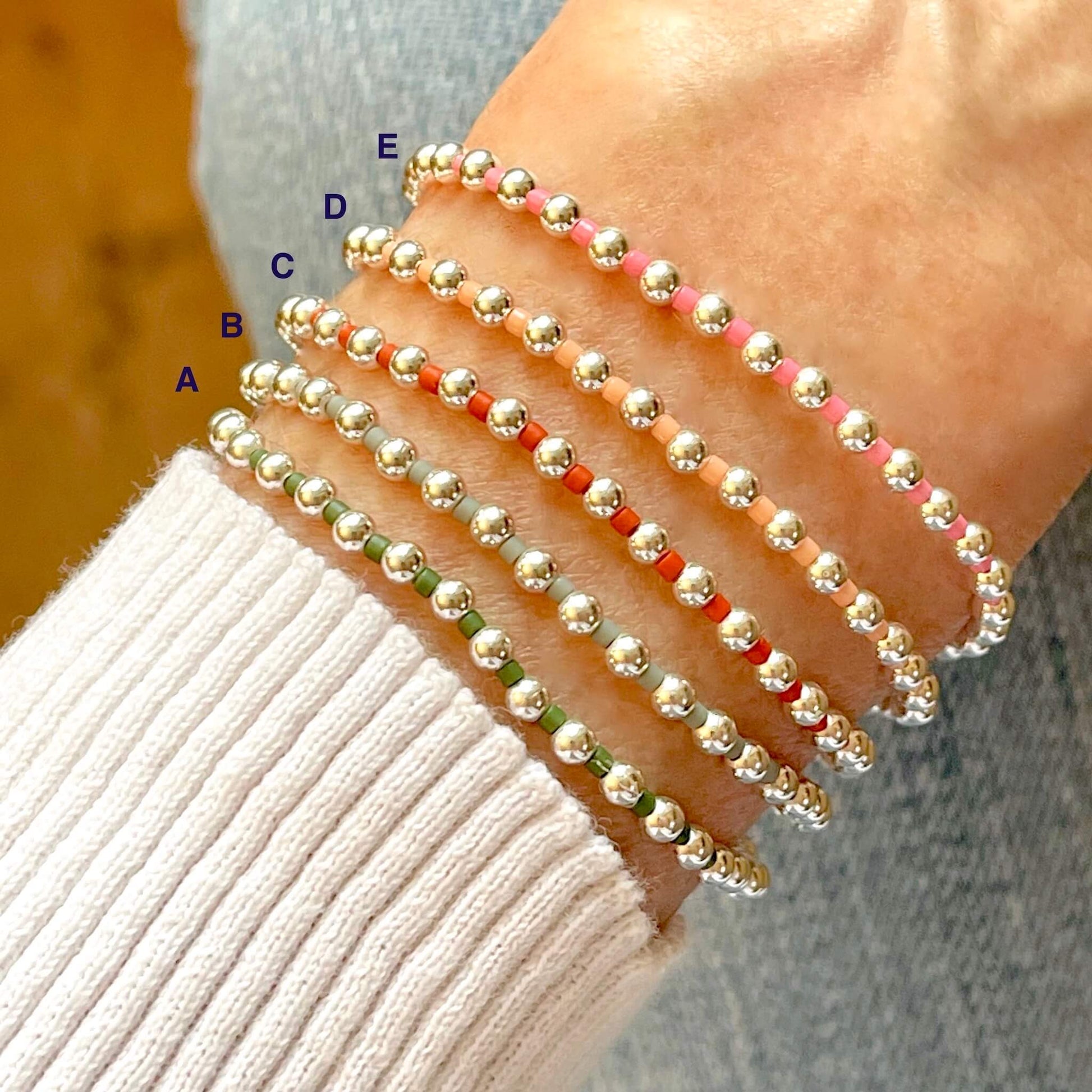 Women's bead bracelets with silver ball beads and alternating seed beads in green, gray, orange, peach, or pink on stretch cord.