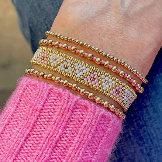 Women's beaded bracelet stack with pink, white, and gold beaded handmade woven and stretch bracelets.