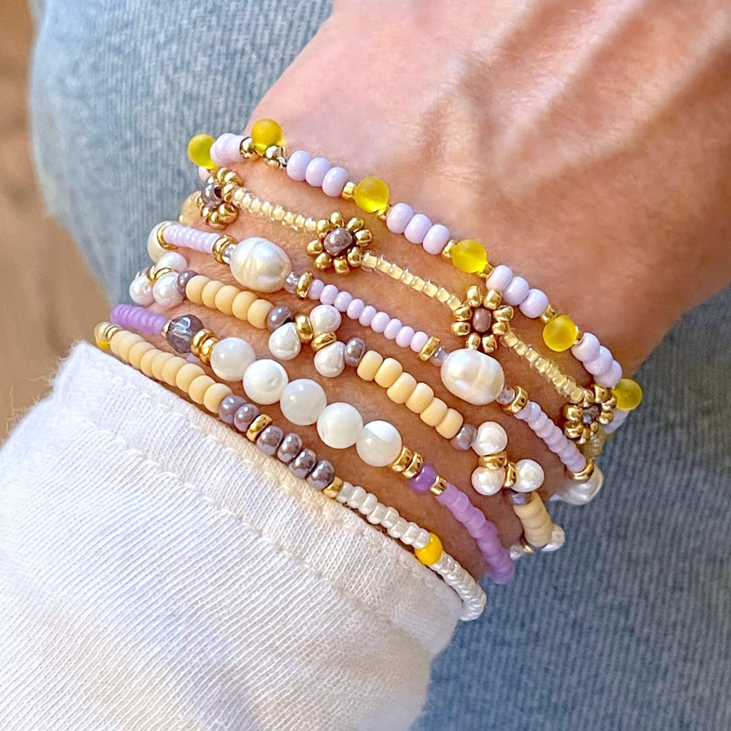 Yellow and lavender beaded bracelets with gold daisy chain flowers. Stack of 6 dainty pastel stretch bracelets with tiny seed beads and pearl beads.
