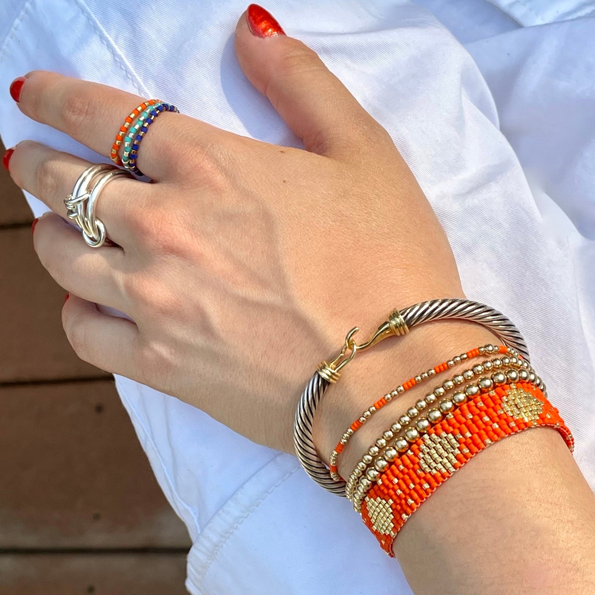 Stack of 3 seed bead stretch rings with alternating metal-tone and orange and blue beads shown on a hand with coordinating bracelets.