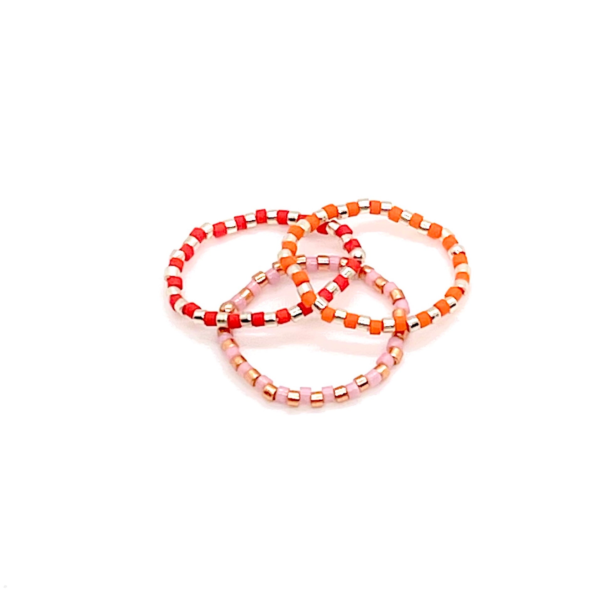 Beaded stretch ring set of 3 with metal-tone, and alternating pink, red, and orange Miyuki Delica seed beads.