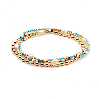 Gold bead bracelet stack with pearls, and blue and peach seed beads on elastic stretch cord.